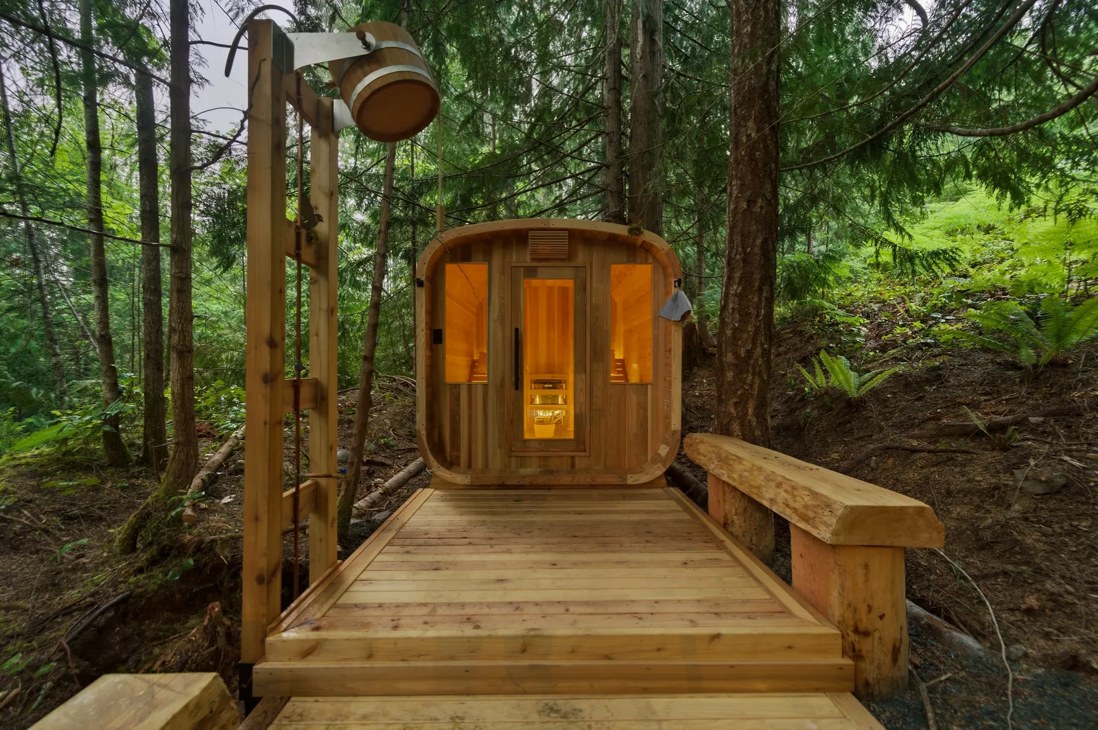 Barrel sauna with glowing windows at the end of a wooden boardwalk